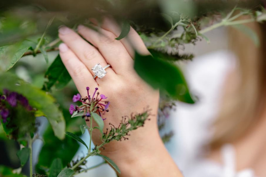 engagement ring on a hand placed against florals and greenery