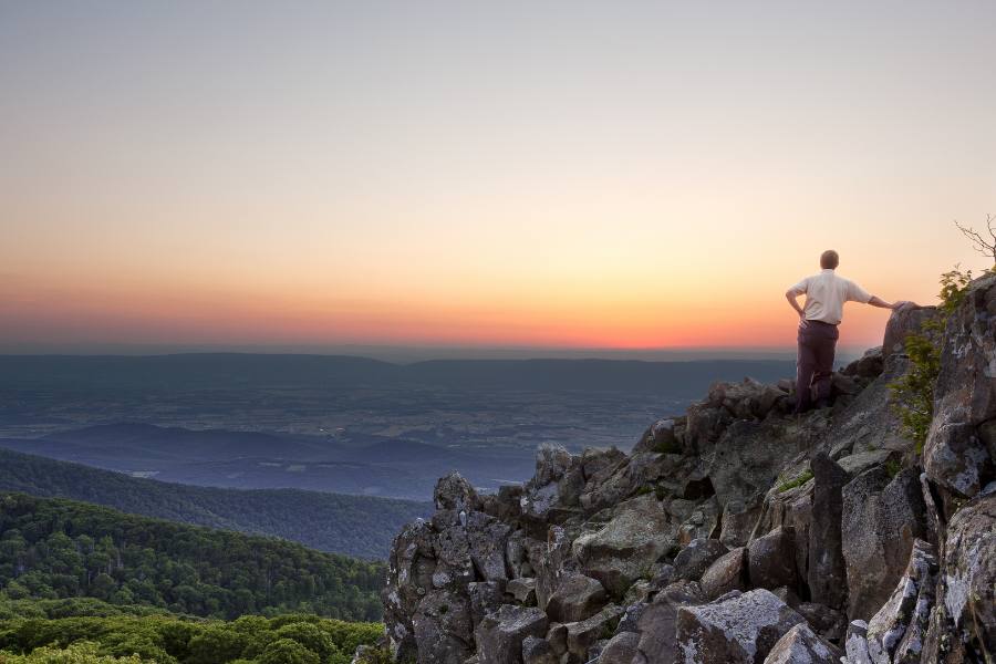Back view of man watching sunset from rocky summit of Stony Man.