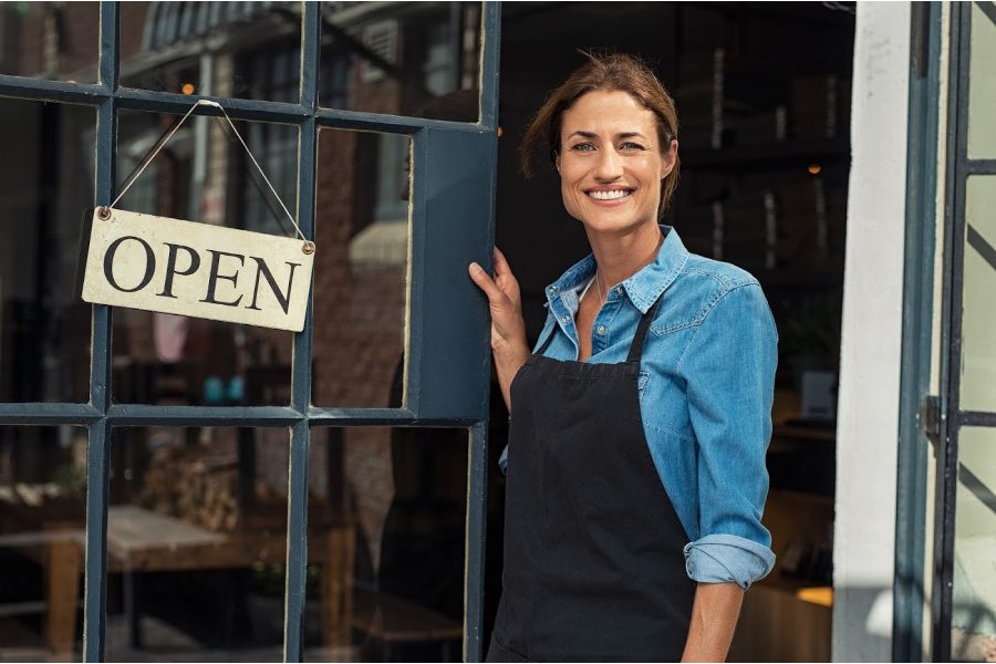 Business owner in front of business with open sign