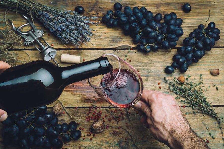 Person pouring wine in a glass over tables with grapes