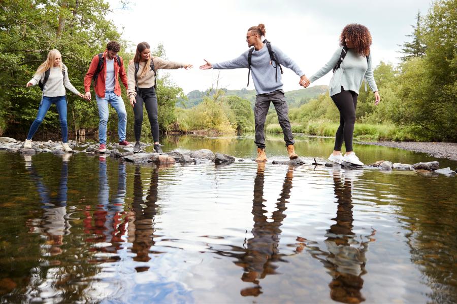 group of hikers walking across rocks through a river 