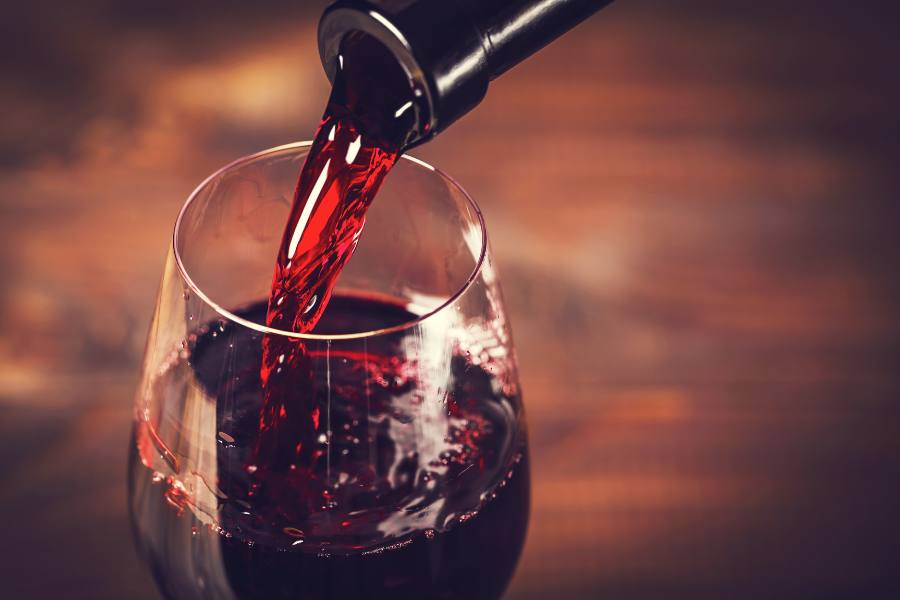 Pouring red wine in a glass in front of a wooden background