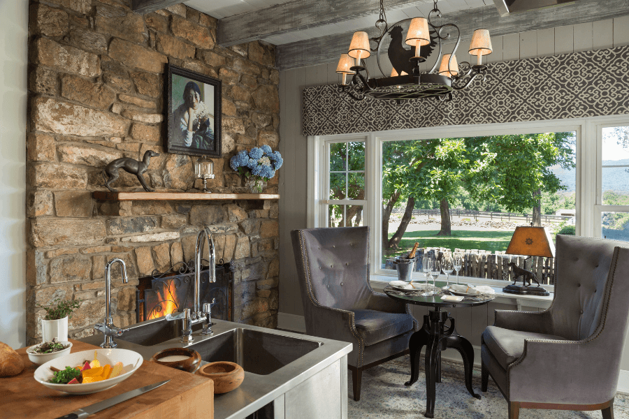 Rustic dining area with a stone fireplace, wingback chairs, and a mountain-view window