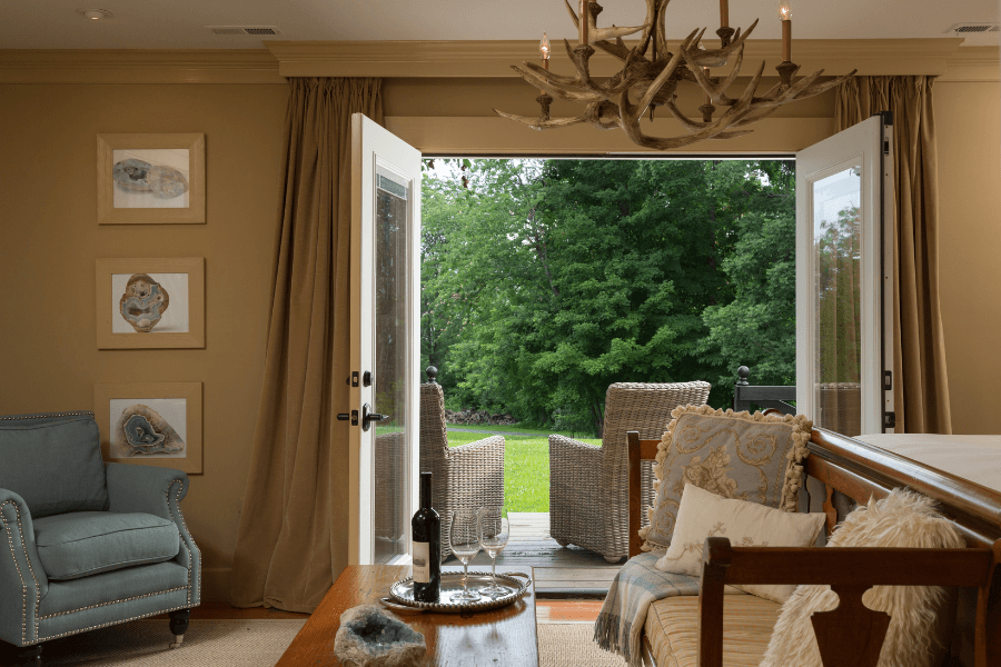 Open French doors leading from a cozy interior to a deck with wicker chairs