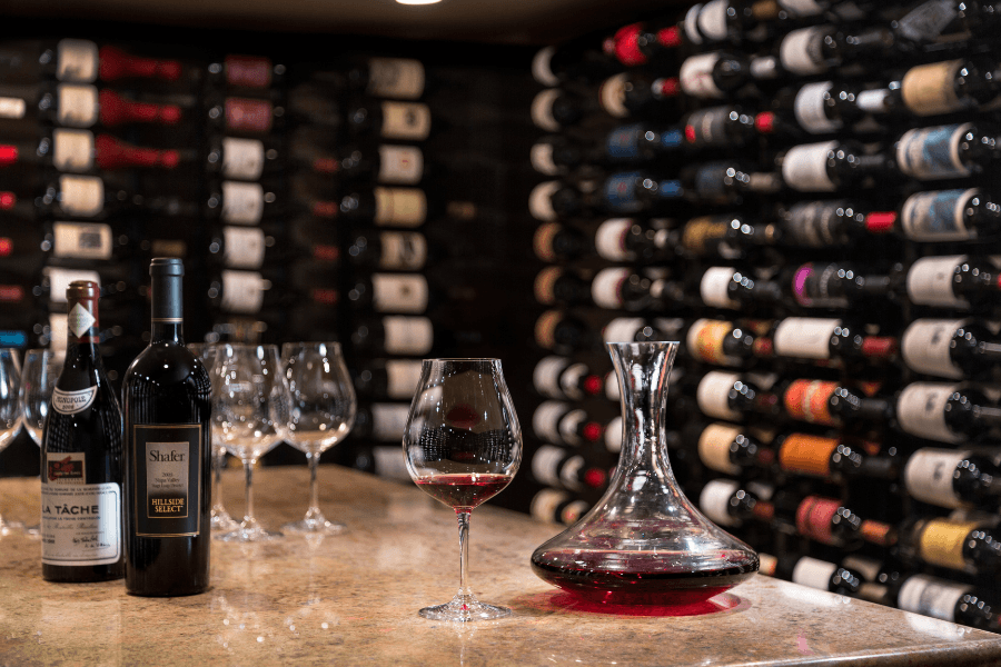 Red wine bottles and a decanter on a counter in a well-stocked wine cellar